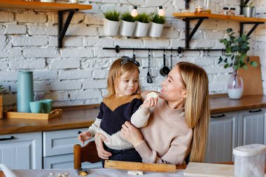 Elinde hamurla oynayan komik küçük bebek yardımcısı mutfakta yoğurmayı öğrenen yetişkin anne, tatlı bebek ve ebeveyn anne kurabiyeleri pişirirken eğleniyor..