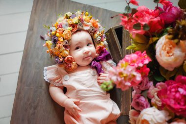 6 aylık güzel bir kız, çiçeklerden yapılmış bir şapkayla sırt üstü yatıyor. Başında çelenkle çiçeklerin arasında küçük bir çocuk..