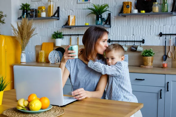 A young woman works at home with a laptop with a child. Home office with children. My mother works at home.