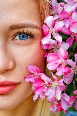 Yüzünün yanında pembe kiraz çiçeği açan bir kadının büyük bir portresi. Mavi gözlü bir sarışın baharda kiraz çiçeklerinin kokusundan hoşlanır. Güzel portre..