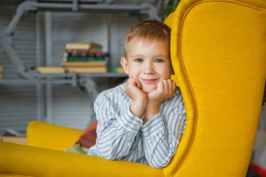Sarı sandalyedeki küçük sarışın bir çocuğun portresi. Kameraya gülümseyerek bakıyor, elleri başının üstünde. Uluslararası Çocuk Günü