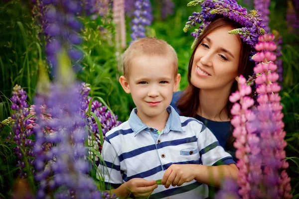 Family outdoor recreation on weekends. A happy mother and a cute baby son are hugging tightly among wild flowers in a field. Maternal happiness. Mother\'s Day. Bouquet for mom