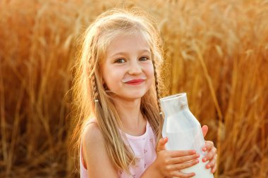 Cam şişeden süt içen, buğday tarlasında ekmek yiyen küçük sarışın bir kızın yakın çekimi. Seçici odak
