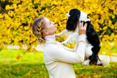 Beyaz saçlı bir kız Cavalier King Charles Spaniel köpeğini kollarında tutuyor. Sonbahar güneşli ormanında bir köpekle yürüyüş. Sağlıklı bir yaşam tarzı. Evcil hayvanlara bakıyorum..