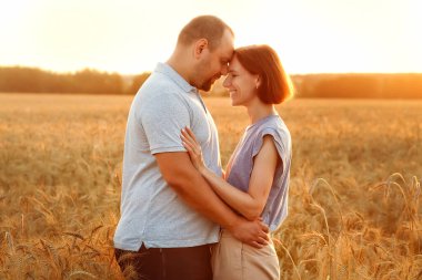 Bir erkek ve bir kadın, buğday tarlasında batan güneşin arka planına sarılıyorlar. Birbirlerine bakıyorlar. Aşıklar yazın gün batımında doğada.
