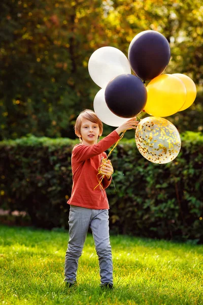 一个拿着气球的孩子正在户外玩耍 一个红头发的男孩在一个阳光灿烂的公园里 在草地上 拿着色彩艳丽的气球 — 图库照片