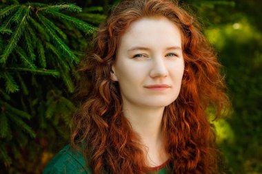 Parktaki yeşilliğin arka planında güzel kızıl saçlı bir kadının büyük bir portresi..