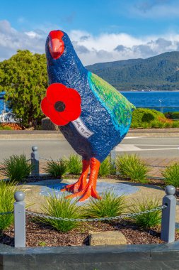 Te Anau, Southland, Yeni Zelanda. Te Anau Gölü 'nün önünde nesli tükenmekte olan bir yerli kuşun dev heykeli. Anzak Günü anısına dev bir haşhaş takıyor. 25 Nisan 2021