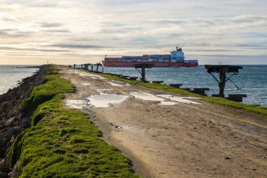 Aramoana Köstebeği 'nin yanından geçen bir konteynır gemisi Yeni Zelanda' nın güneyindeki Aramoana köyünün yanında okyanusta uzun bir dalgakıran.