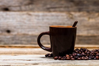 Ahşap masa ve arka planda izole edilmiş kahve fincanının yanında kavrulmuş kahve çekirdekleri..