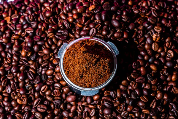 Background with ground coffee in portafilter surrounded by roasted coffee beans,