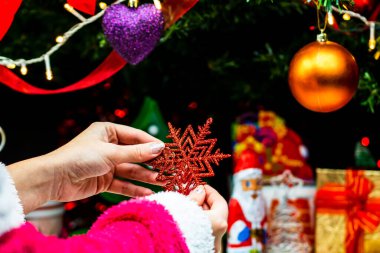 Noel ağacının önünde Noel süsü tutan eller. Noel süslemeleri ile köknar dallarını süslemek.