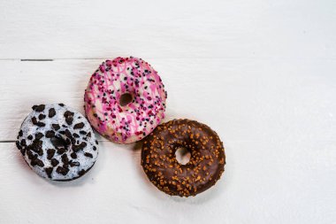 Beyaz ahşap masada renkli çörekler. Şekerli, şekerli, şekerli, şekerli, şekerli. Kopyalama alanı olan üst görünüm