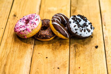 Ahşap masada renkli çörekler. Jöleli şekerli tatlı yiyecekler, çikolatalı donutlar. Kopyalama alanı olan üst görünüm