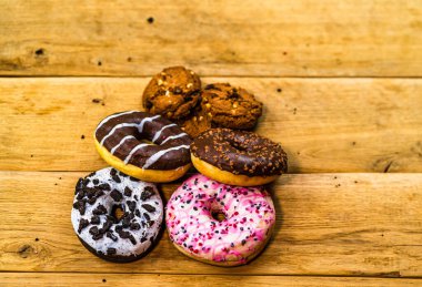 Ahşap masada renkli çörekler ve bisküviler. Jöleli şekerli tatlı yiyecekler, çikolatalı donutlar. Kopyalama alanı olan üst görünüm
