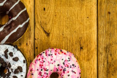 Ahşap masada renkli çörekler. Jöleli şekerli tatlı yiyecekler, çikolatalı donutlar. Kopyalama alanı olan üst görünüm