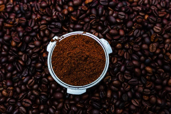 Background with ground coffee in portafilter surrounded by roasted coffee beans,