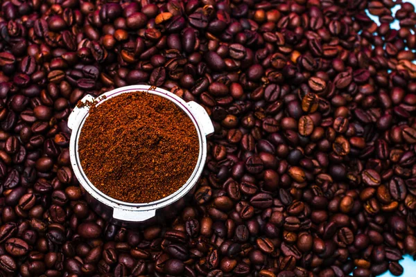 Background with ground coffee in portafilter surrounded by roasted coffee beans,