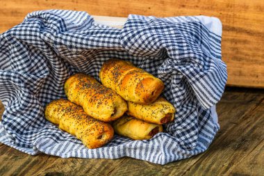 Hamurda pişmiş sosisler tuzlu ve haşhaş tohumlarıyla dolu kırsal bir sepetin içinde. Sosisli börekler, ev yapımı lezzetli hamur işleri..