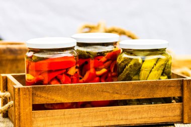 Cam kavanozlu tahta sandık, kırmızı dolma biber turşusu ve salatalık turşusu. Çeşitli sebze turşulu kavanozlar. Kaba bir kompozisyonda yiyecek konseptini korudu.