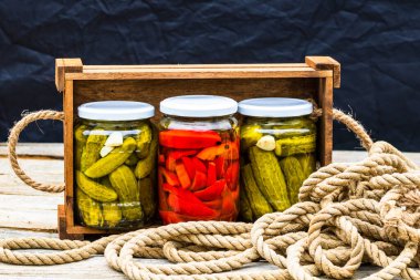 Cam kavanozlu tahta sandık, kırmızı dolma biber turşusu ve salatalık turşusu. Çeşitli sebze turşulu kavanozlar. Kaba bir kompozisyonda yiyecek konseptini korudu.