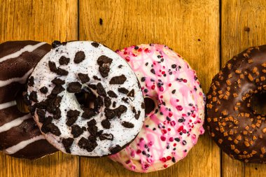 Ahşap masada renkli çörekler. Jöleli şekerli tatlı yiyecekler, çikolatalı donutlar. Kopyalama alanı olan üst görünüm