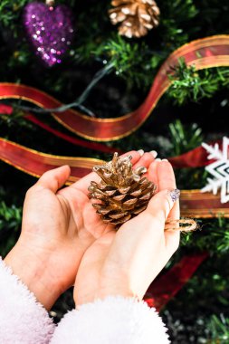 Noel ağacının önünde Noel süsü tutan eller. Noel süslemeleri ile köknar dallarını süslemek.