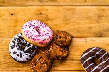 Ahşap masada renkli çörekler. Jöleli şekerli tatlı yiyecekler, çikolatalı donutlar. Kopyalama alanı olan üst görünüm