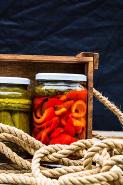 Cam kavanozlu tahta sandık, kırmızı dolma biber turşusu ve salatalık turşusu. Çeşitli sebze turşulu kavanozlar. Kaba bir kompozisyonda yiyecek konseptini korudu.