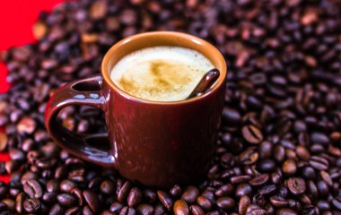 Bir fincan kahve, kırmızı arka planda kavrulmuş kahve çekirdekleri, kahve konsepti, kahve fotografını kapat.