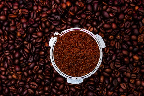 Background with ground coffee in portafilter surrounded by roasted coffee beans,