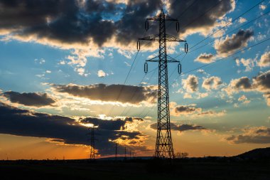 Güzel dramatik gökyüzü ve bulutlar, gün batımının ışıkları iletim kulesinin üzerinde (elektrik direği) bir tarlada.