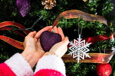 Noel ağacının önünde Noel süsü tutan eller. Noel süslemeleri ile köknar dallarını süslemek.