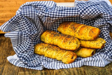Hamurda pişmiş sosisler tuzlu ve haşhaş tohumlarıyla dolu kırsal bir sepetin içinde. Sosisli börekler, ev yapımı lezzetli hamur işleri..
