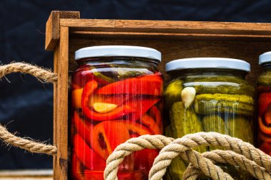 Cam kavanozlu tahta sandık, kırmızı dolma biber turşusu ve salatalık turşusu. Çeşitli sebze turşulu kavanozlar. Kaba bir kompozisyonda yiyecek konseptini korudu.