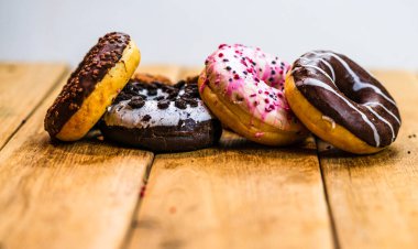 Ahşap masada renkli çörekler. Jöleli şekerli tatlı yiyecekler, çikolatalı donutlar. Kopyalama alanı olan üst görünüm