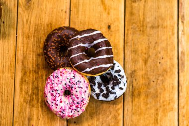 Ahşap masada renkli çörekler. Jöleli şekerli tatlı yiyecekler, çikolatalı donutlar. Kopyalama alanı olan üst görünüm