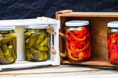 Cam kavanozlu tahta sandık, kırmızı dolma biber turşusu ve salatalık turşusu. Çeşitli sebze turşulu kavanozlar. Kaba bir kompozisyonda yiyecek konseptini korudu.