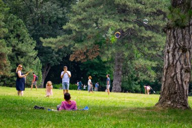 Annesi küçük kızı için sabun köpükleri yapıyor, insanlar piknik yapıyor ve parkta Coronavirus krizi sırasında eğleniyorlar ve Romanya 'nın Bükreş kentindeki Mogosoaia bölgesinin bahçeleri, 2020.