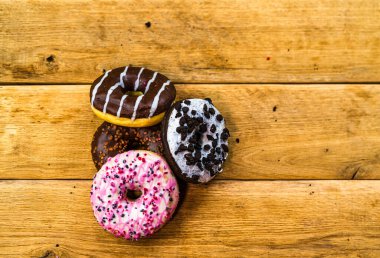 Ahşap masada renkli çörekler. Jöleli şekerli tatlı yiyecekler, çikolatalı donutlar. Kopyalama alanı olan üst görünüm