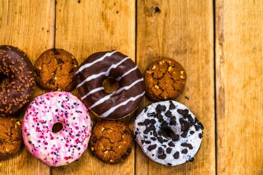 Ahşap masada renkli çörekler. Jöleli şekerli tatlı yiyecekler, çikolatalı donutlar. Kopyalama alanı olan üst görünüm