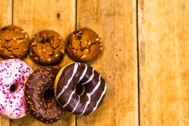 Ahşap masada renkli çörekler. Jöleli şekerli tatlı yiyecekler, çikolatalı donutlar. Kopyalama alanı olan üst görünüm