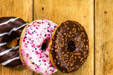 Ahşap masada renkli çörekler. Jöleli şekerli tatlı yiyecekler, çikolatalı donutlar. Kopyalama alanı olan üst görünüm