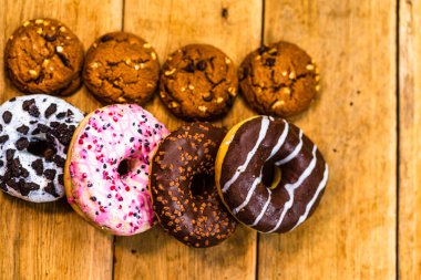 Ahşap masada renkli çörekler. Jöleli şekerli tatlı yiyecekler, çikolatalı donutlar. Kopyalama alanı olan üst görünüm