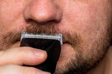 Adam saç makası kullanarak sakalını tıraş ediyor ya da kesiyor.