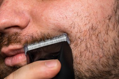 Adam saç makası kullanarak sakalını tıraş ediyor ya da kesiyor.