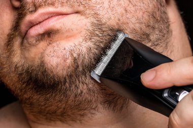 Adam saç makası kullanarak sakalını tıraş ediyor ya da kesiyor.