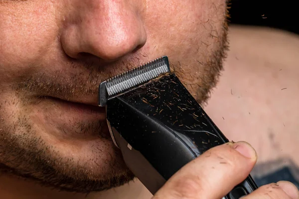 Adam saç makası kullanarak sakalını tıraş ediyor ya da kesiyor.