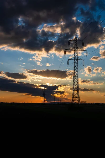 Güzel dramatik gökyüzü ve bulutlar, gün batımının ışıkları iletim kulesinin üzerinde (elektrik direği) bir tarlada.