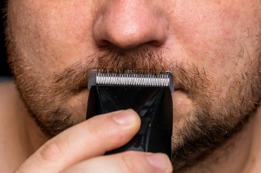 Adam saç makası kullanarak sakalını tıraş ediyor ya da kesiyor.